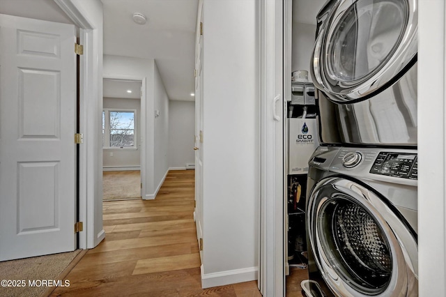 laundry room featuring a baseboard radiator, laundry area, baseboards, stacked washer / drying machine, and light wood-type flooring