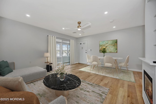 living area with a ceiling fan, a glass covered fireplace, light wood-style flooring, and recessed lighting