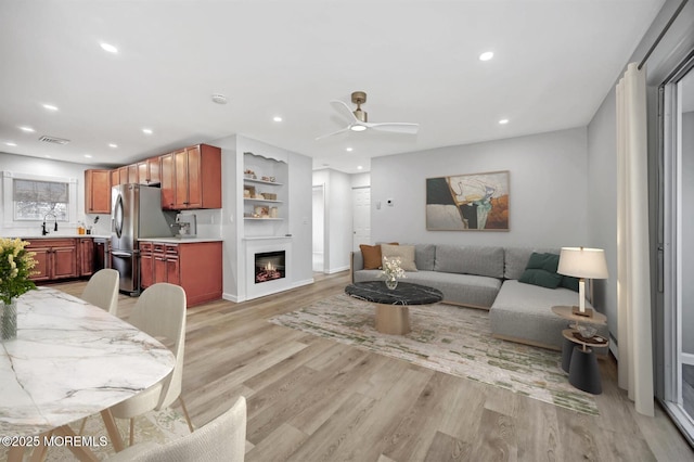 living area with recessed lighting, visible vents, a ceiling fan, light wood-type flooring, and a glass covered fireplace