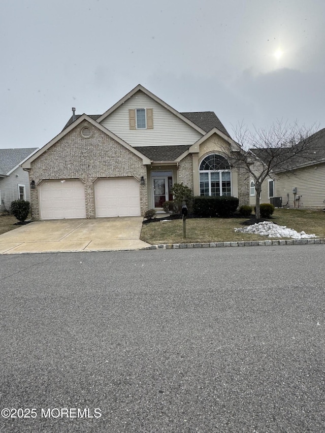 view of front of property featuring brick siding, a shingled roof, a garage, cooling unit, and driveway