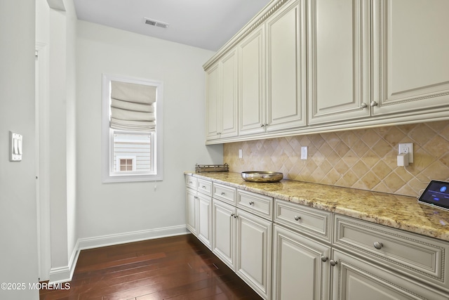 kitchen featuring dark hardwood / wood-style floors, backsplash, light stone counters, and cream cabinetry