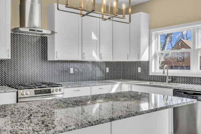 kitchen with white cabinetry, light stone counters, decorative light fixtures, appliances with stainless steel finishes, and range hood