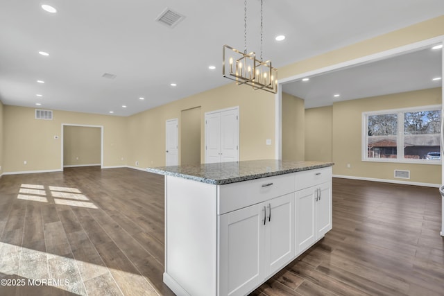 kitchen with a center island, dark hardwood / wood-style flooring, pendant lighting, dark stone counters, and white cabinets