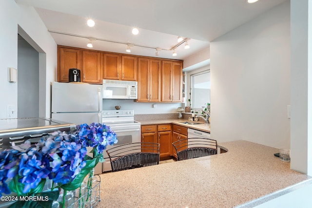 kitchen with a peninsula, white appliances, a sink, and brown cabinets