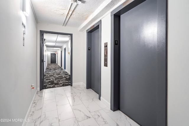 hallway featuring a textured ceiling, marble finish floor, baseboards, and elevator