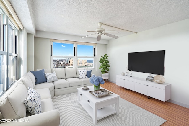 living area featuring a textured ceiling, wood finished floors, a ceiling fan, and baseboards