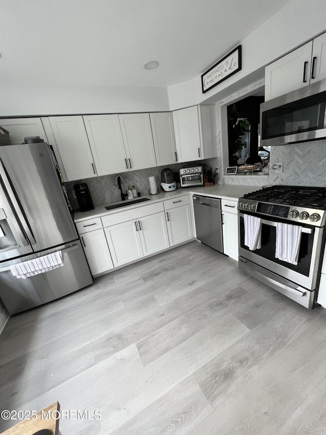 kitchen featuring a sink, stainless steel appliances, light countertops, white cabinetry, and backsplash