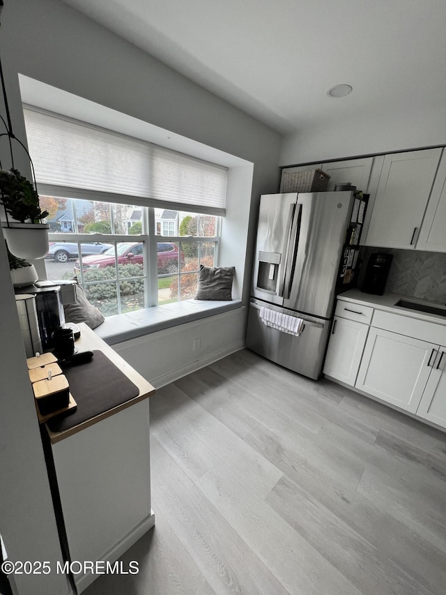 kitchen with tasteful backsplash, light wood-style floors, white cabinets, and stainless steel refrigerator with ice dispenser