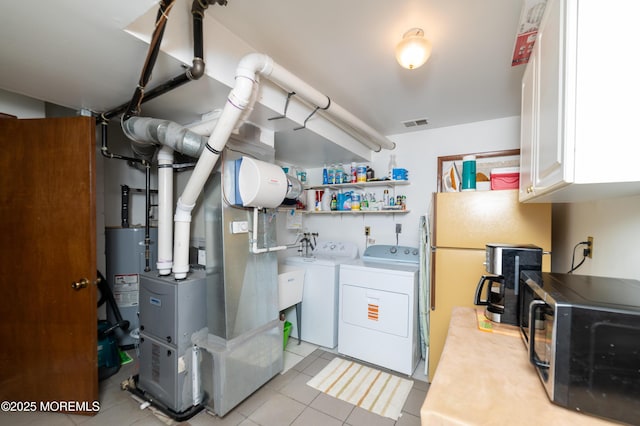 washroom with water heater, washer and dryer, light tile patterned floors, and cabinets