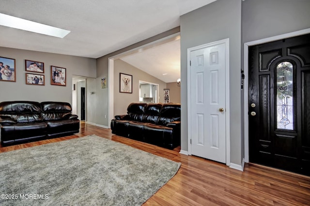 living area featuring lofted ceiling with skylight, baseboards, and wood finished floors