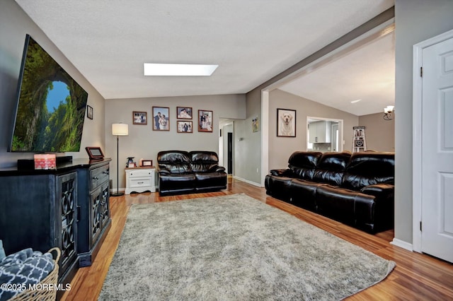 living area with lofted ceiling with skylight, baseboards, and light wood finished floors