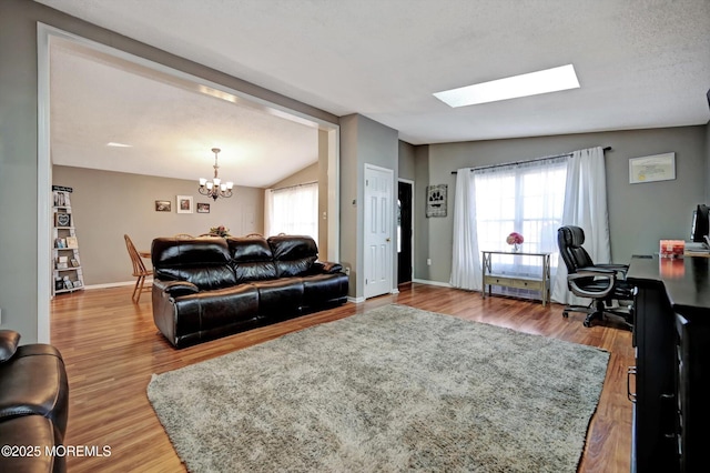 living room with lofted ceiling with skylight, baseboards, an inviting chandelier, and wood finished floors