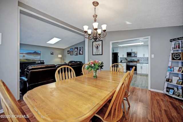 dining room featuring a notable chandelier, vaulted ceiling, baseboards, and wood finished floors