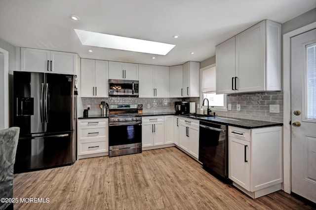 kitchen with stainless steel appliances, dark countertops, white cabinetry, and a sink