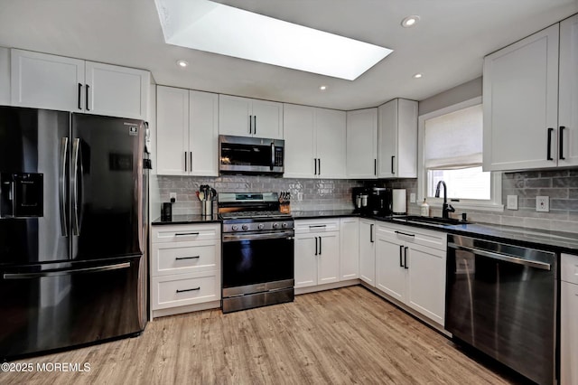 kitchen featuring dark countertops, stainless steel appliances, light wood-type flooring, white cabinetry, and a sink