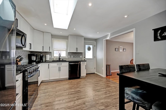 kitchen with a skylight, black gas range oven, dishwashing machine, dark countertops, and a sink