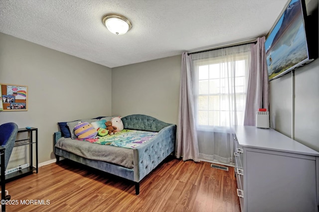 bedroom featuring light wood-type flooring, visible vents, a textured ceiling, and baseboards