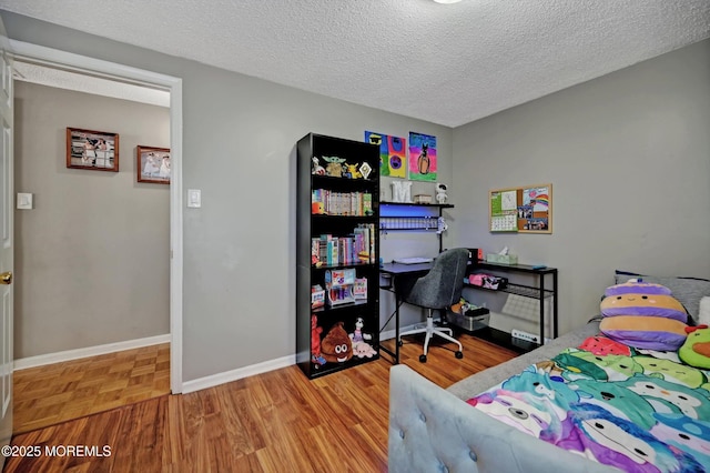 bedroom with a textured ceiling, baseboards, and wood finished floors