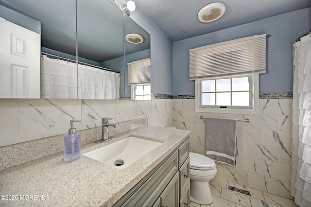 full bath with visible vents, toilet, marble finish floor, vanity, and tile walls