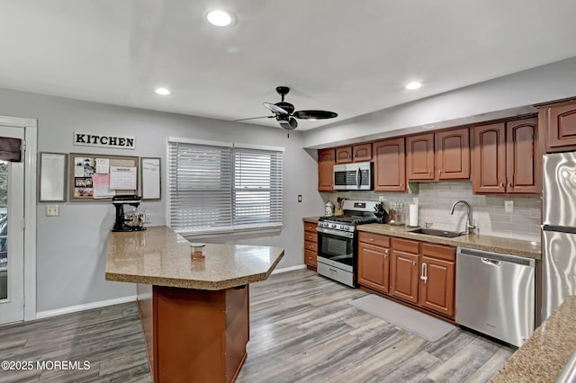 kitchen with sink, backsplash, stainless steel appliances, light hardwood / wood-style floors, and kitchen peninsula