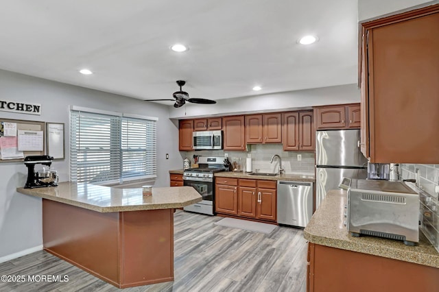 kitchen with stainless steel appliances, sink, light hardwood / wood-style floors, and kitchen peninsula