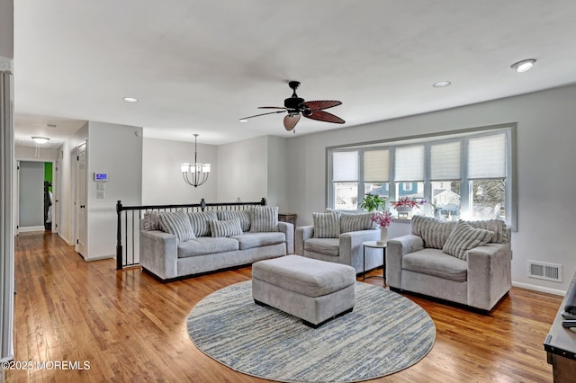 living room featuring ceiling fan with notable chandelier and light hardwood / wood-style flooring