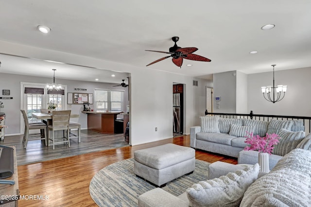 living room featuring ceiling fan with notable chandelier and light hardwood / wood-style flooring