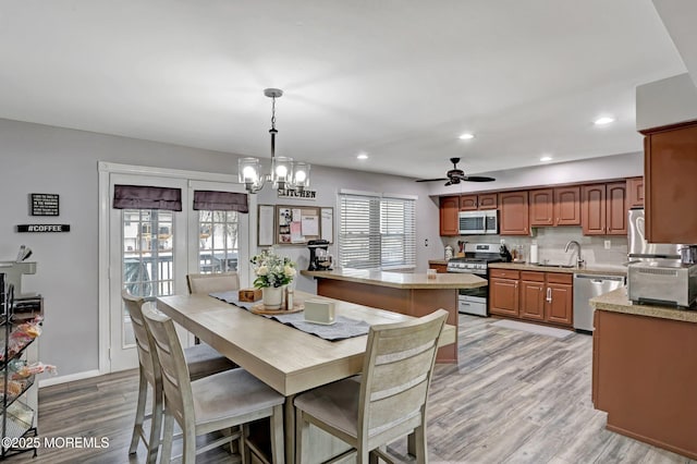 dining area with sink, ceiling fan with notable chandelier, and light wood-type flooring