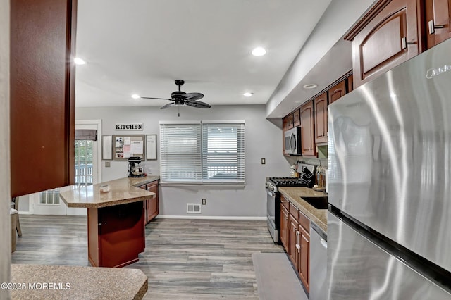 kitchen featuring ceiling fan, appliances with stainless steel finishes, a kitchen bar, and light wood-type flooring