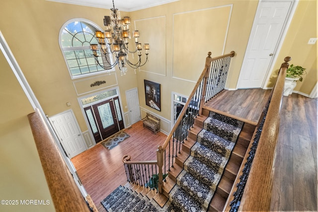 foyer entrance with stairway, ornamental molding, wood finished floors, a high ceiling, and a notable chandelier