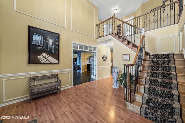 stairway featuring a decorative wall, wood finished floors, a towering ceiling, wainscoting, and crown molding