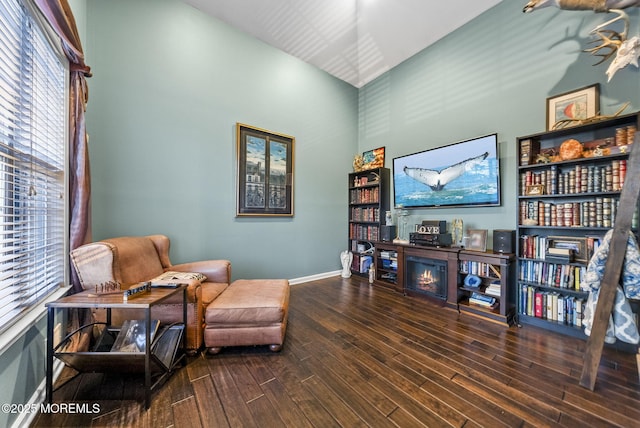 living area with a lit fireplace, a high ceiling, baseboards, and wood finished floors