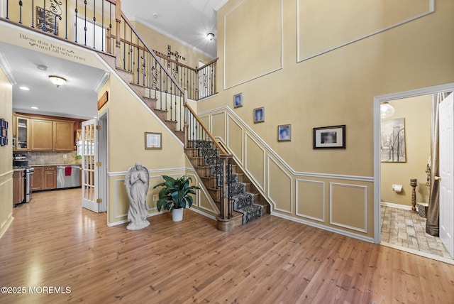 stairway with wainscoting, a towering ceiling, ornamental molding, wood finished floors, and a decorative wall