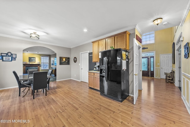 kitchen featuring light wood-style floors, arched walkways, crown molding, and black fridge with ice dispenser