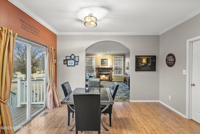 dining space with a warm lit fireplace, visible vents, baseboards, light wood-type flooring, and crown molding