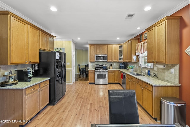 kitchen featuring light stone counters, ornamental molding, stainless steel appliances, and a sink