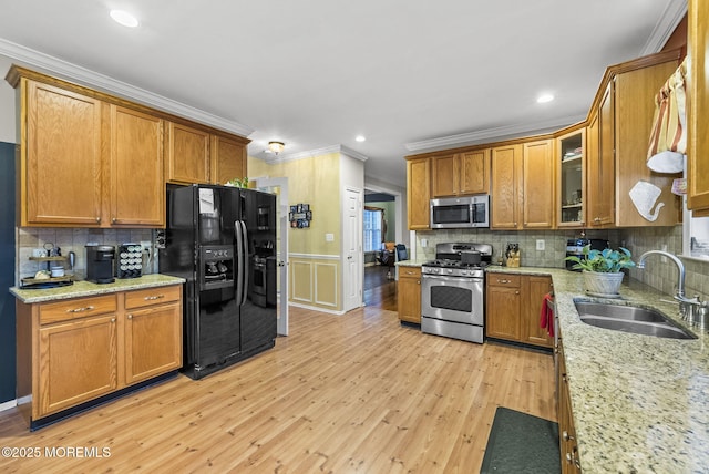 kitchen featuring stainless steel appliances, light wood-style flooring, brown cabinetry, ornamental molding, and a sink