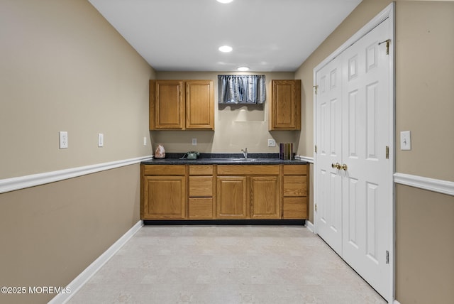 kitchen featuring brown cabinets, dark countertops, recessed lighting, a sink, and baseboards