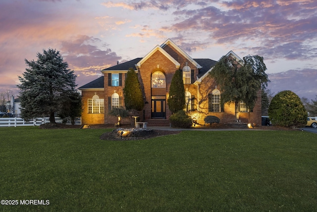 view of front facade featuring brick siding, fence, and a front yard