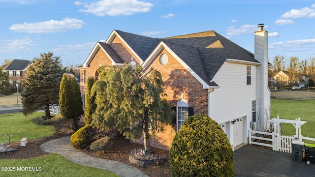 view of home's exterior with a garage, brick siding, fence, a yard, and a chimney