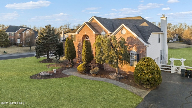 view of front of house with a front yard, brick siding, fence, and a chimney