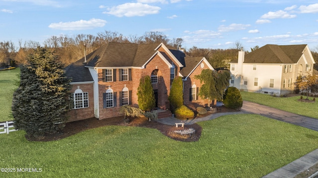 view of front of property featuring brick siding, fence, a front lawn, and roof with shingles