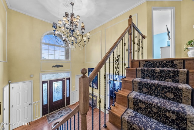 foyer entrance featuring stairs, ornamental molding, wood finished floors, and an inviting chandelier