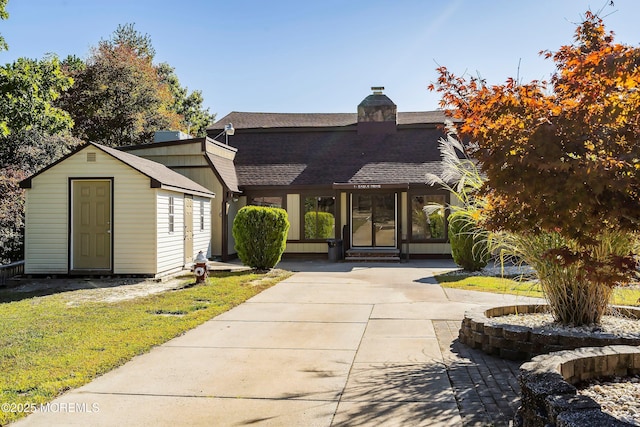 exterior space featuring a storage shed, an outdoor structure, roof with shingles, a chimney, and a front yard