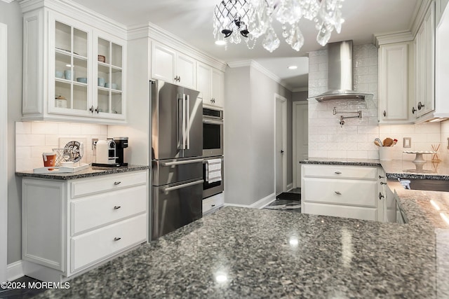 kitchen featuring stainless steel appliances, white cabinets, decorative backsplash, dark stone counters, and wall chimney exhaust hood