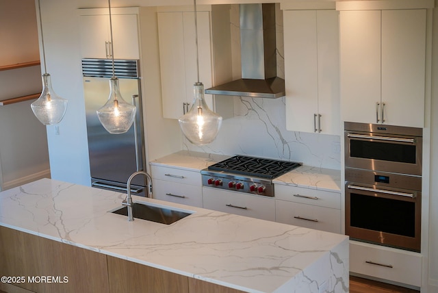 kitchen featuring sink, appliances with stainless steel finishes, light stone countertops, an island with sink, and wall chimney exhaust hood