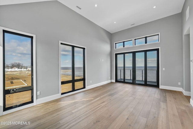 unfurnished room featuring french doors, a water view, light hardwood / wood-style floors, and a high ceiling