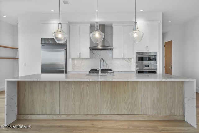 kitchen featuring white cabinetry, a large island with sink, stainless steel appliances, and wall chimney exhaust hood