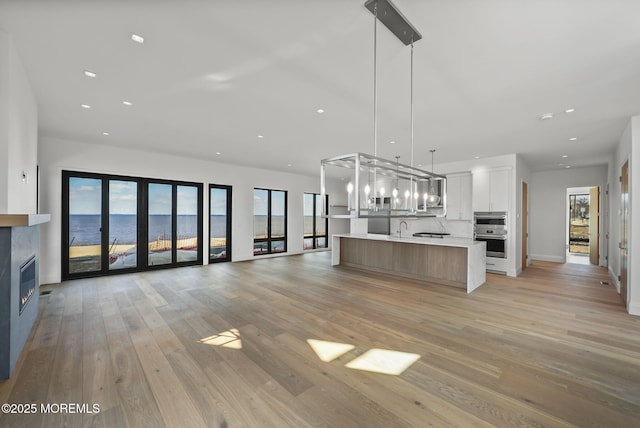 kitchen featuring pendant lighting, white cabinets, a large island with sink, light hardwood / wood-style floors, and a water view