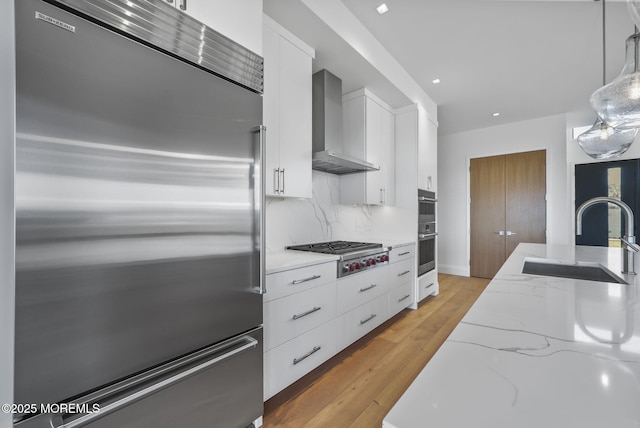 kitchen featuring pendant lighting, sink, appliances with stainless steel finishes, white cabinetry, and wall chimney exhaust hood